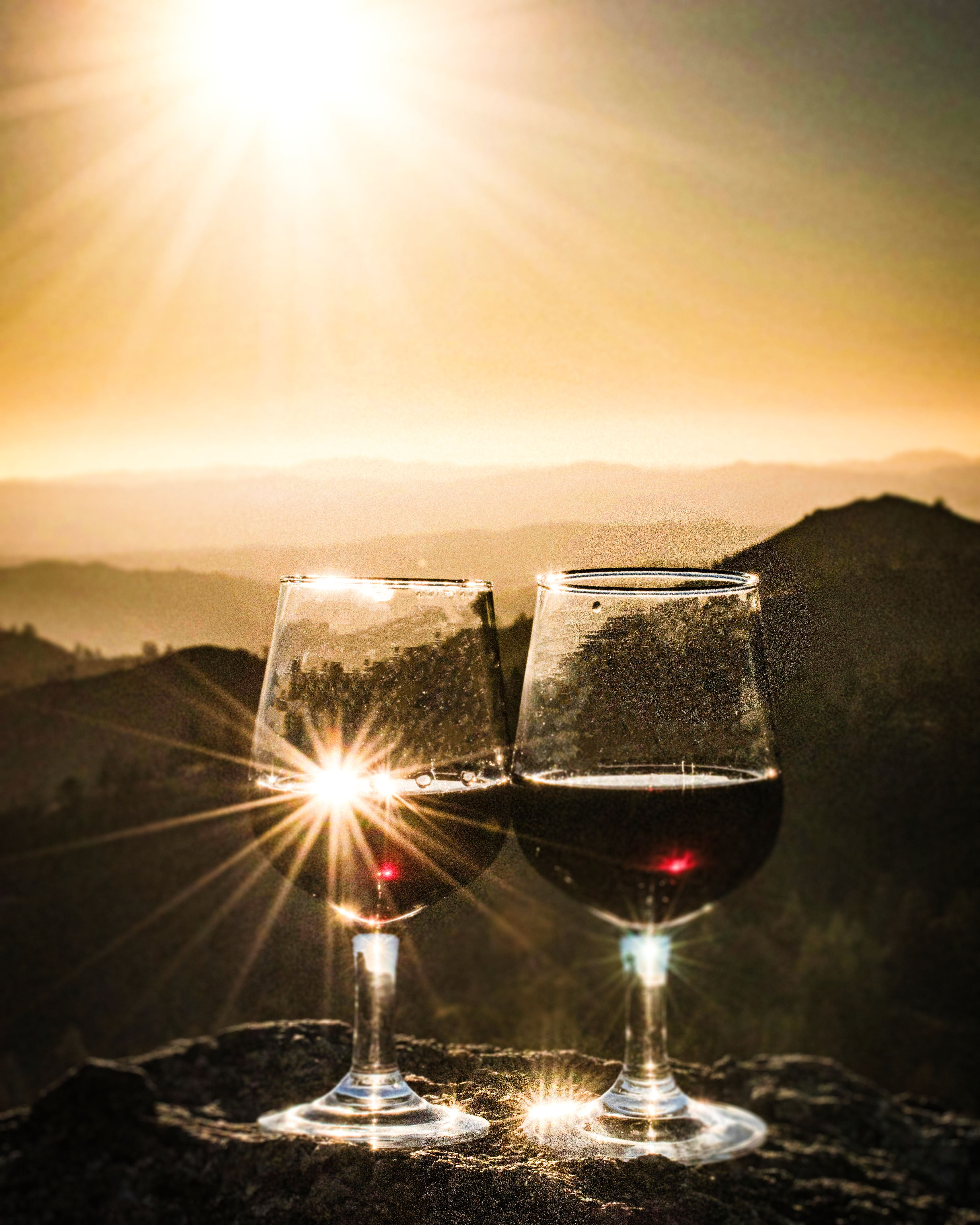 Two wine glasses with red wine against a sunset mountain backdrop